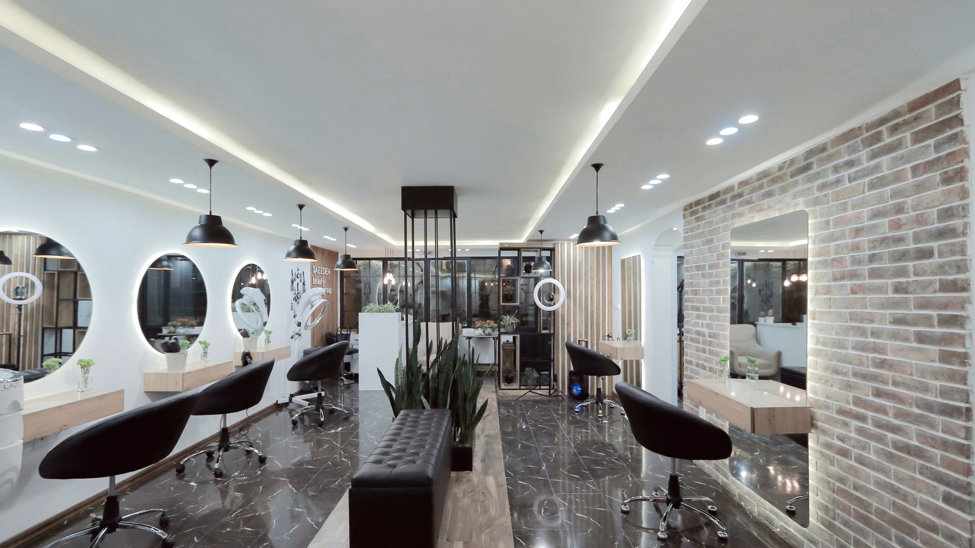 Interior do salão com espelhos redondos iluminados, cadeiras pretas e chão de mármore escuro