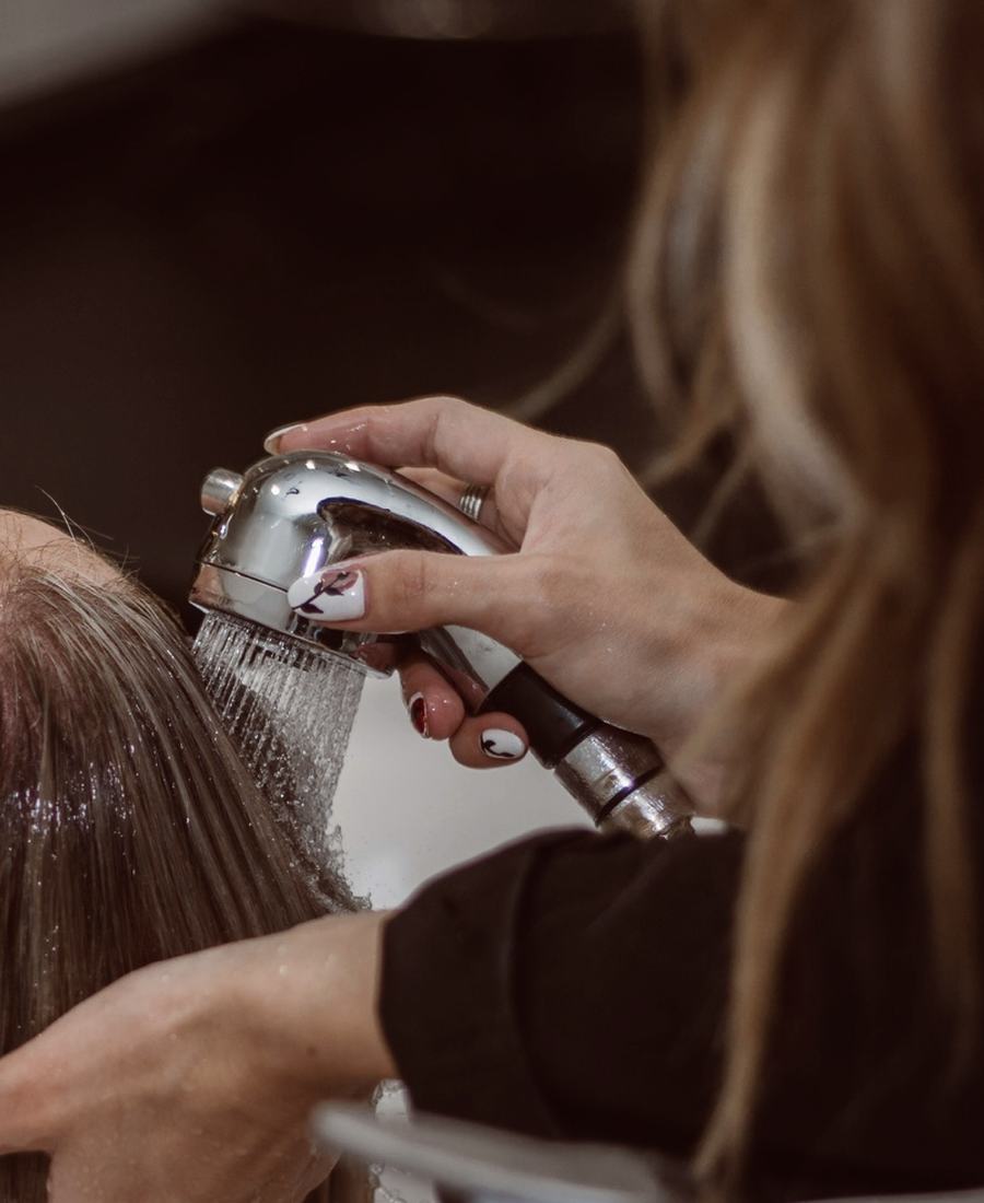 Mãos a lavar o cabelo com o chuveiro do lavatório